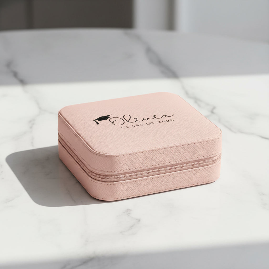 Pink jewelry box with 'Olivia Class of 2026' text and graduation cap design on a white marble table