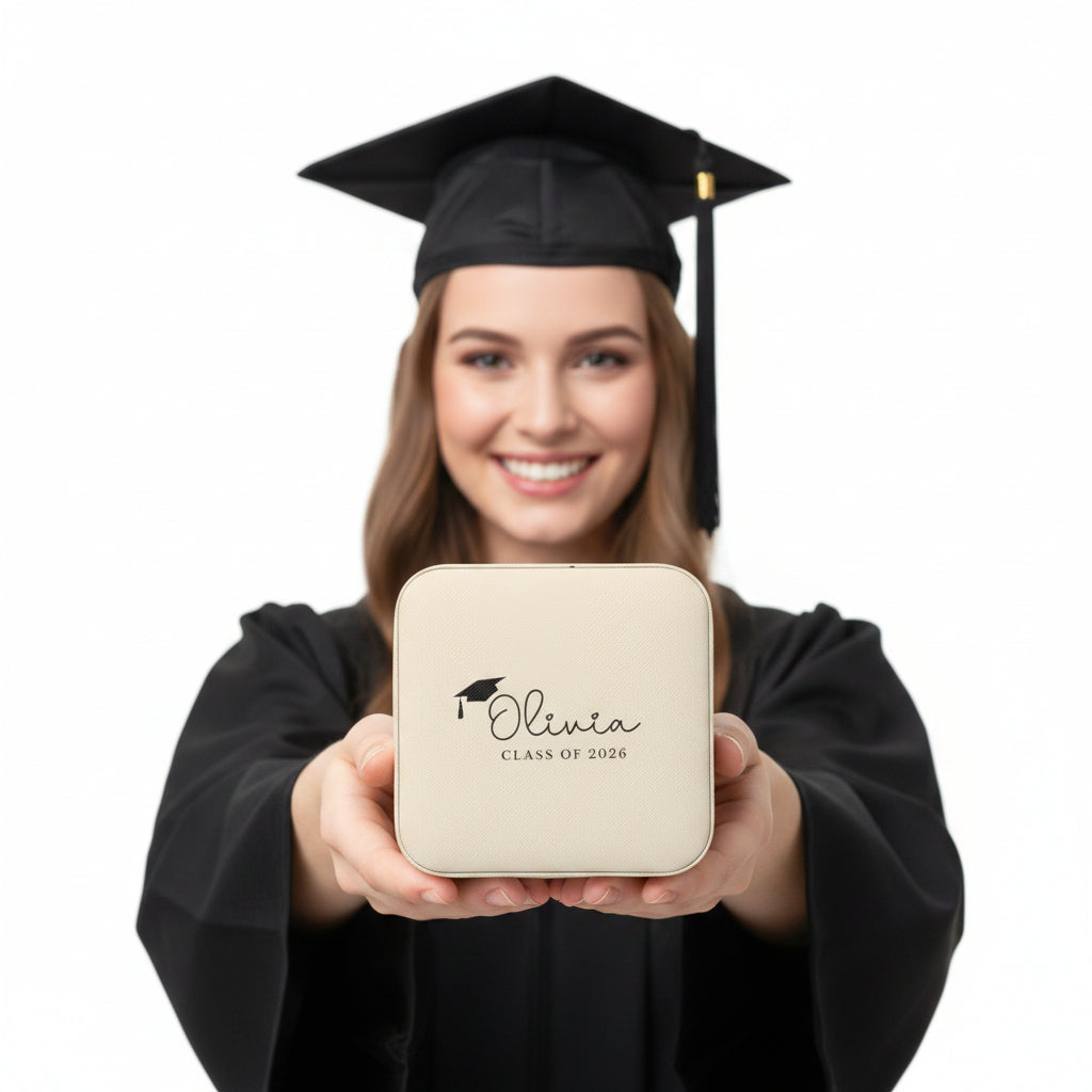 Beige jewelry box with 'Olivia Class of 2026' engraving held in a hand on a white background